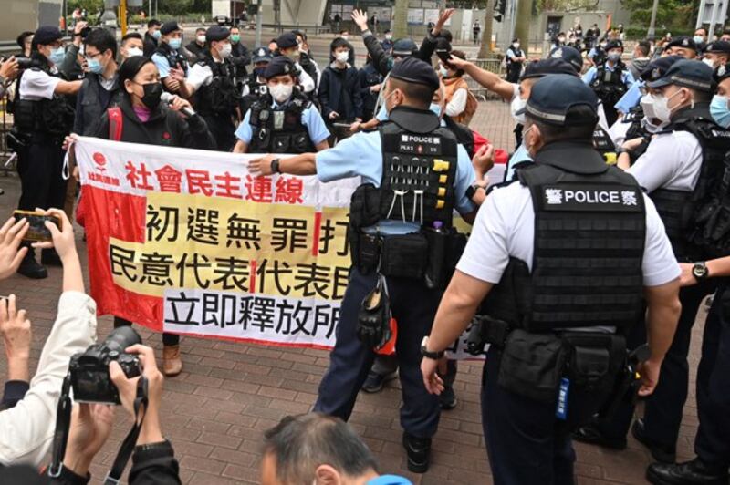 Members of the League of Social Democrats are surrounded by police as they carry a banner outside a court in Hong Kong on February 6, 2023, as the trial of 47 of Hong Kong's most prominent pro-democracy figures begins in the largest prosecution under a national security law that has crushed dissent in the city. Credit: AFP